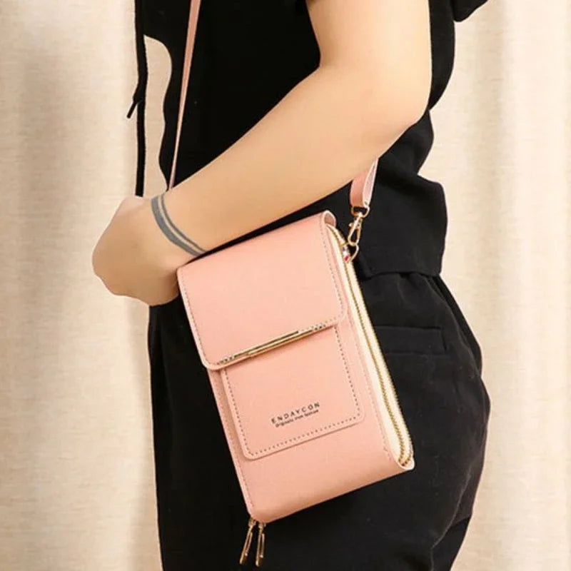 A light pink women's touch screen crossbody shoulder bag carried by a person wearing a black top and pants.