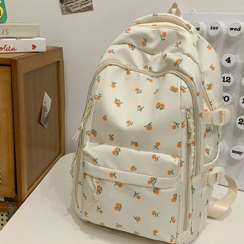 Mochila de color crema con estampado floral de hojas naranjas y verdes, sobre fondo blanco.