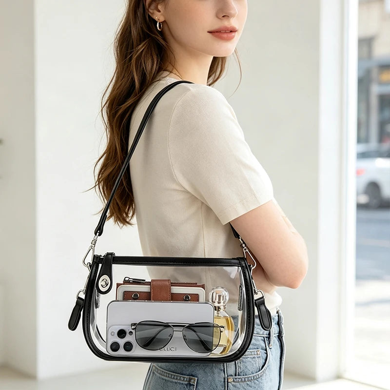 Une femme tient un sac à l'épaule en PVC transparent avec une sangle en cuir marron et un smartphone dedans.
