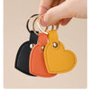 A hand is holding a gold-ringed leather heart keychain in black, orange, and yellow colors.