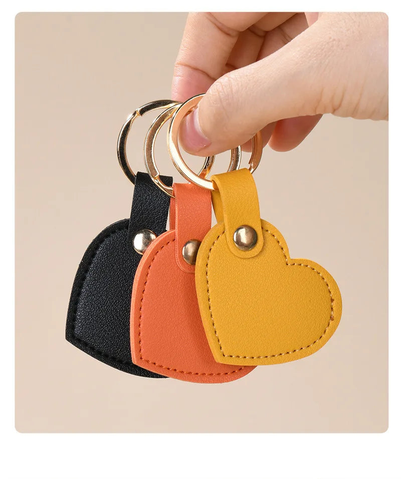 A hand is holding a gold-ringed leather heart keychain in black, orange, and yellow colors.