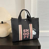 A black canvas shoulder bag featuring a Snoopy cartoon design with pink and beige stripes, displayed on a dark surface.