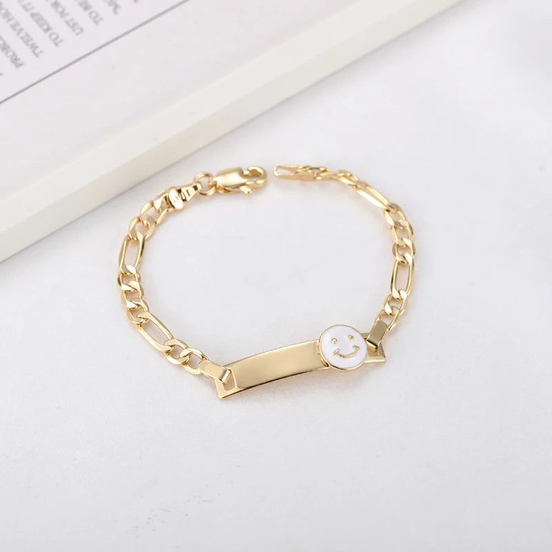 A gold-colored chain bracelet with a smiling face charm on a white background.