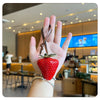 Une main tient un porte-clés de charm à forme de fraise rouge dans un café.