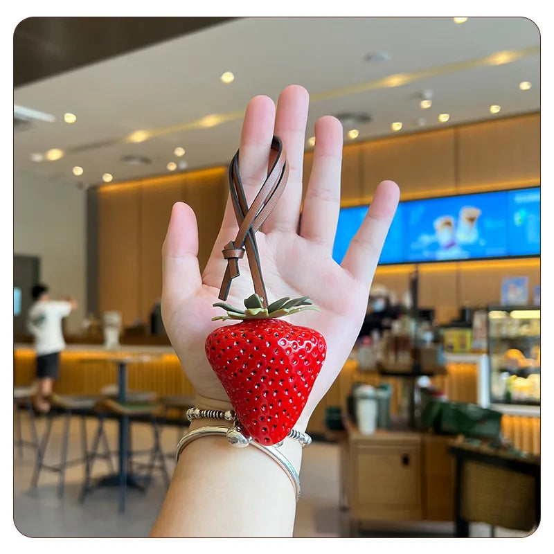 Une main tient un porte-clés de charm à forme de fraise rouge dans un café.