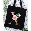 Black canvas tote bag featuring a large gold letter X design with pink floral accents.