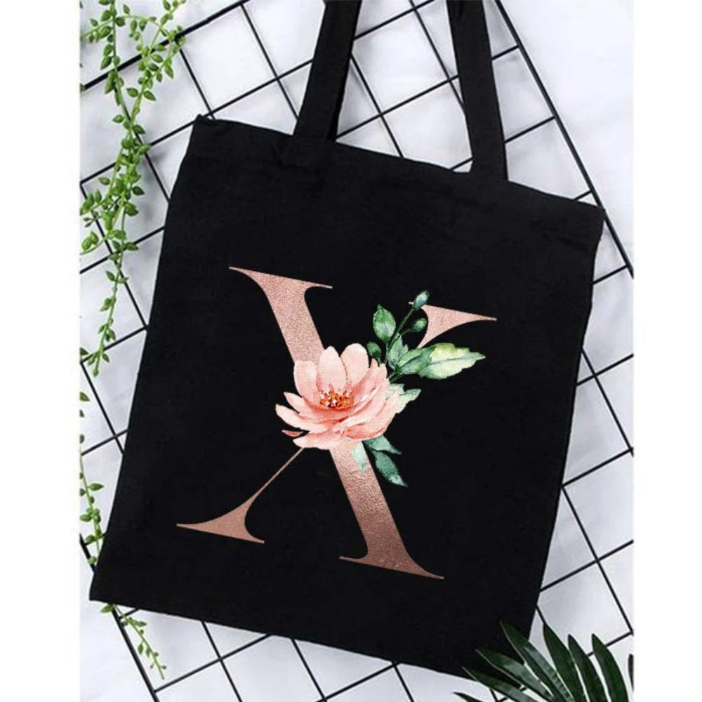Black canvas tote bag featuring a large gold letter X design with pink floral accents.