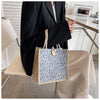 A beige floral linen tote bag with blue accents is held by a person in a black blazer.