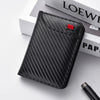 A black carbon fiber texture slim bi-fold wallet resting on a white surface next to a book.