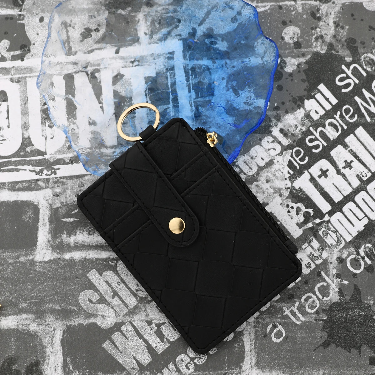 Black PU leather card holder wallet with a gold bangle and tassel resting on a textured surface.