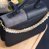 A dark gray and black leather shoulder bag with a gold pearl chain strap resting on a wooden surface.