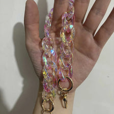 A hand holds a long, iridescent pink and yellow resin chain strap with a gold charm.