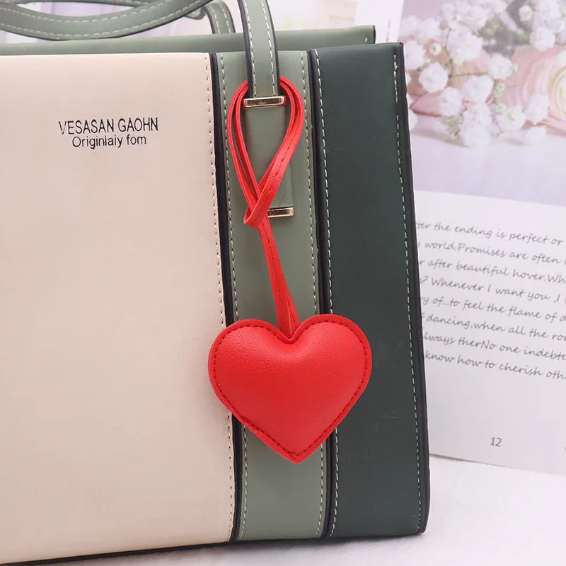 A light beige leather pouch with a dark green trim and a red heart keychain charm.