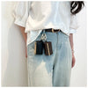 A close-up of a woman wearing a white shirt and light wash jeans with a brown leather belt and a black mini keychain attached