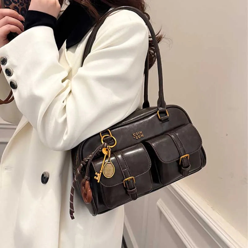 Una mujer sostiene un bolso de hombro de cuero PU marrón oscuro retro con herrajes dorados contra un fondo claro.