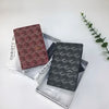 A pair of geometric print passport wallets in maroon and gray are displayed in a silver tray on a white surface.