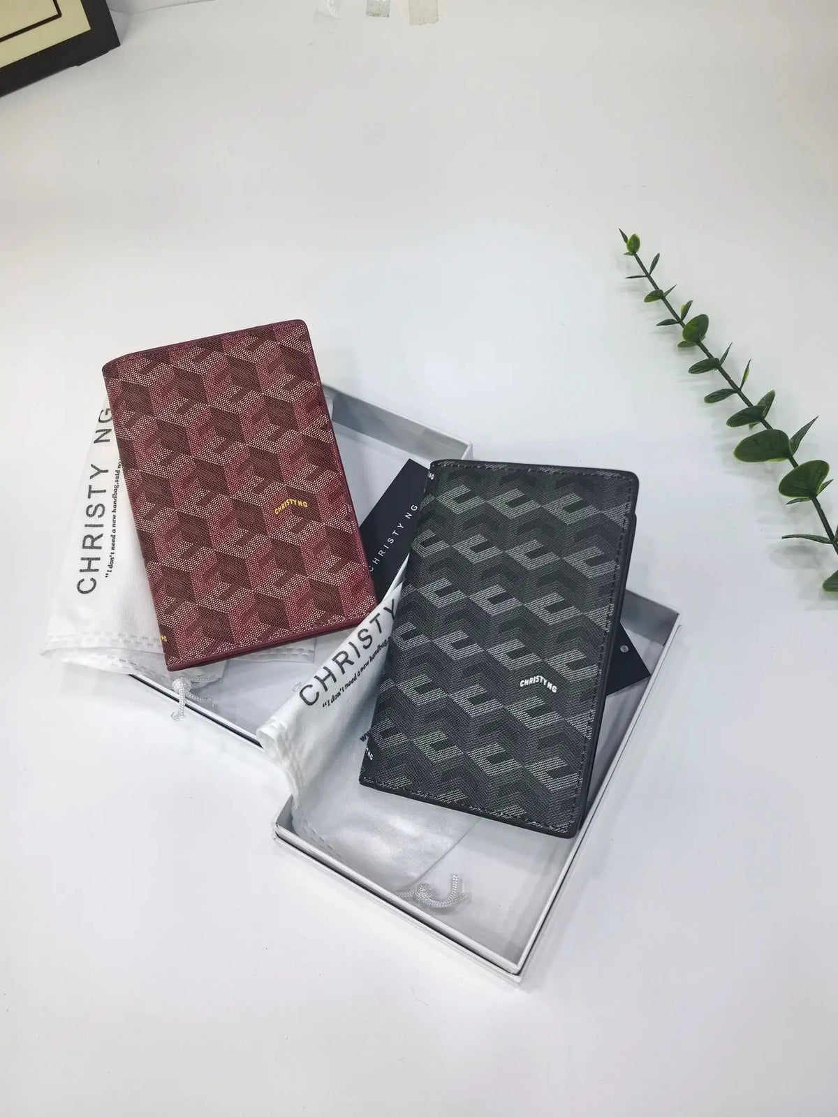 A pair of geometric print passport wallets in maroon and gray are displayed in a silver tray on a white surface.