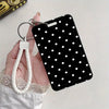 A black card holder with white polka dots attached to a silver metal keyring and lanyard, held by a hand.