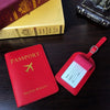 A red PU leather passport wallet and a pink passport holder are displayed on a dark wooden surface next to old books.