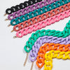 A display of colorful matte acrylic choker necklaces in various shades including black, purple, teal, pink, and orange.