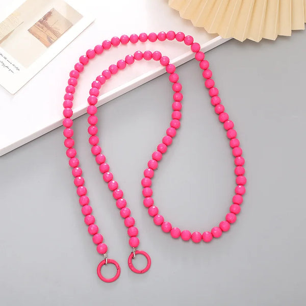 Pink acrylic bead cross phone charm necklace laid on a gray surface with a light background.