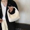 A person holds a cream woven embossed hobo shoulder bag with a top handle against a white background.