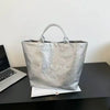 Silver transparent waterproof PVC tote bag with handles resting on a dark surface.