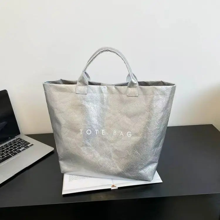 Silver transparent waterproof PVC tote bag with handles resting on a dark surface.