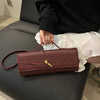 A person holds a burgundy crocodile-embossed PU leather clutch bag with a gold clasp on a gray couch.