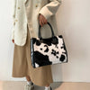 A woman holds a black and white leopard print faux fur designer shoulder tote bag while wearing a beige coat and skirt.