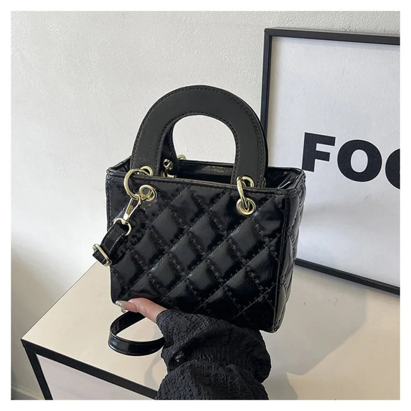 A black quilted diamond grid textured crossbody bag with gold hardware displayed against a white background.