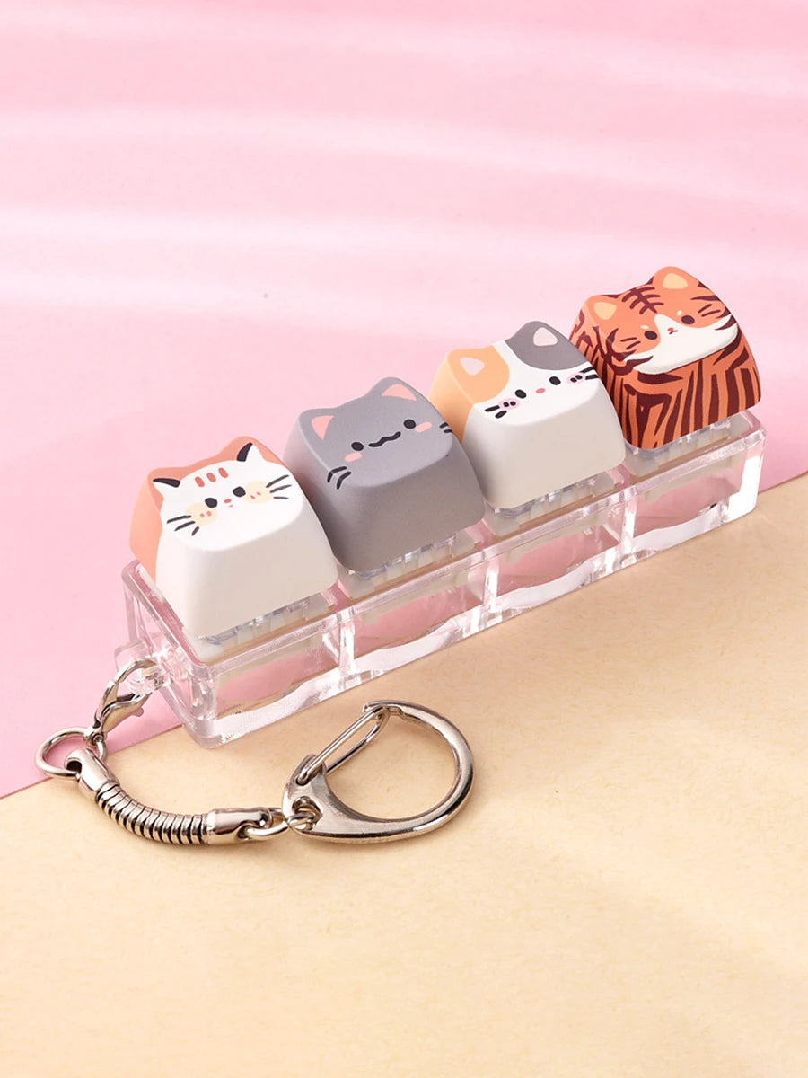 A set of acrylic kawaii cat keycaps and fidget toys displayed on a clear plastic tray with a silver bag charm.