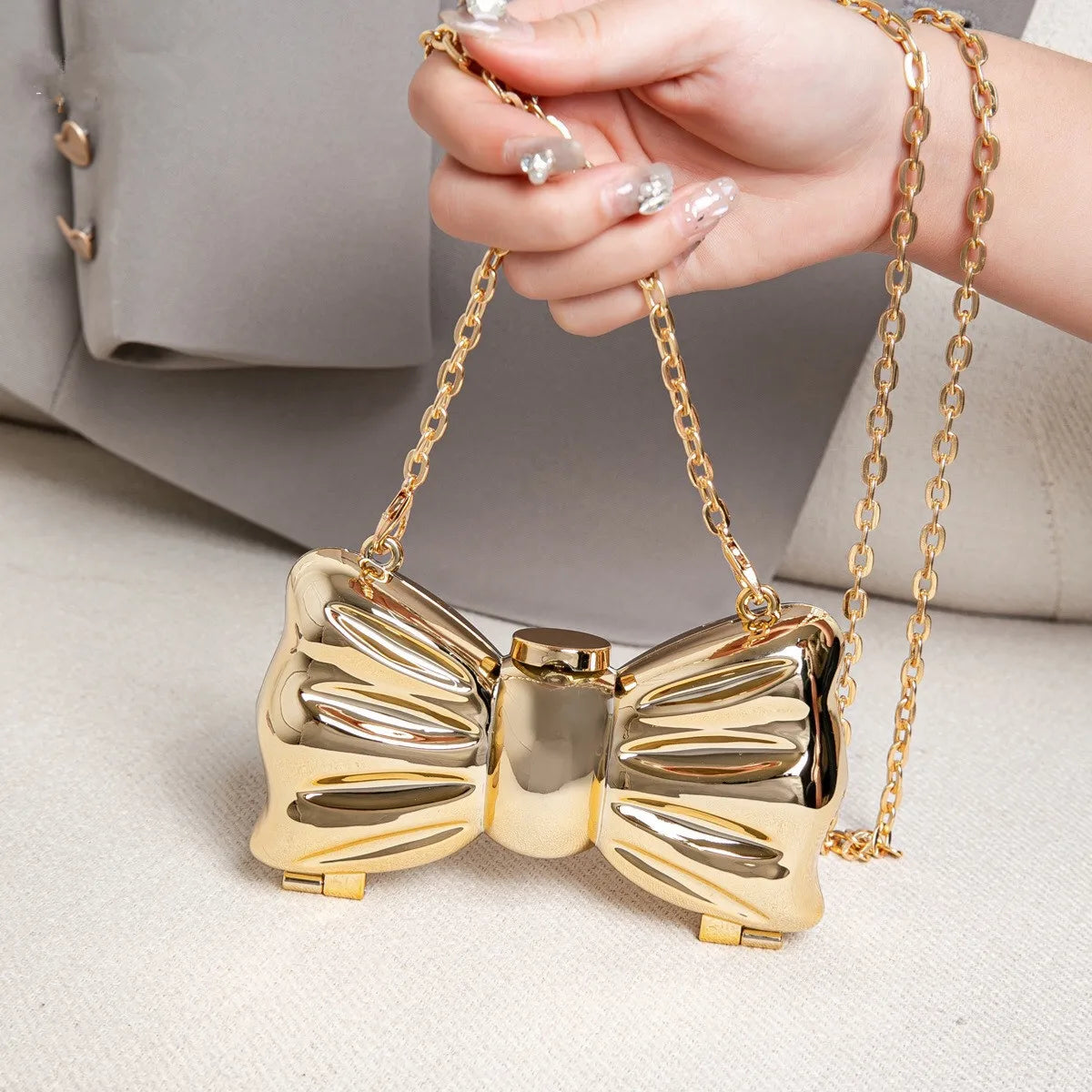A hand holds a gold heart-shaped acrylic evening clutch with a chain strap on a light surface.