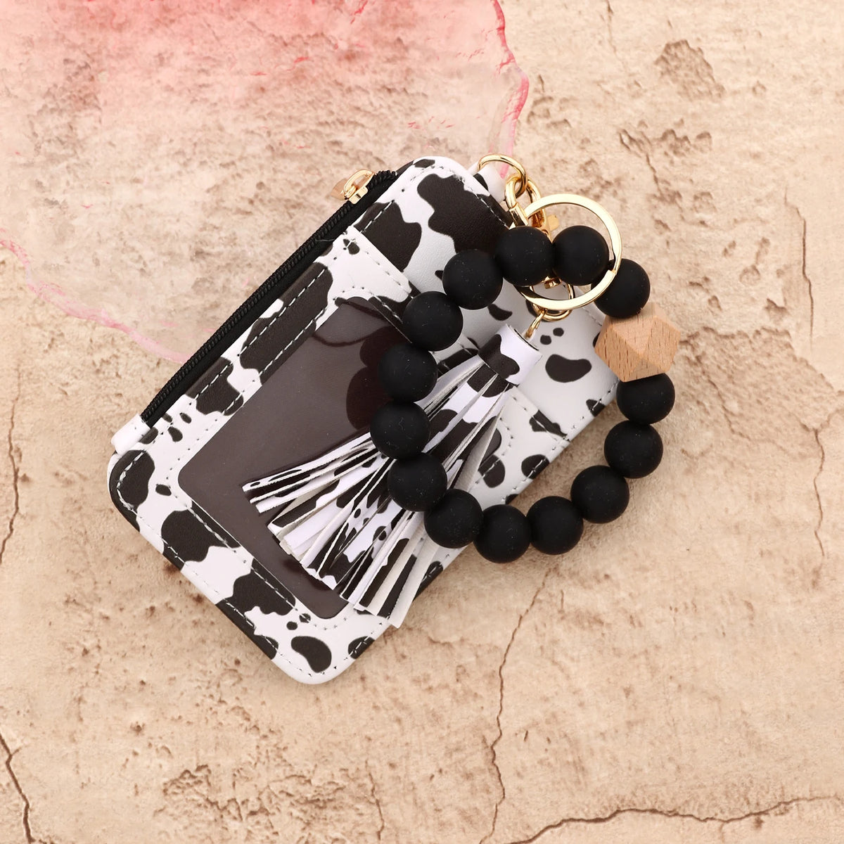 A black and white leopard print leather card holder with a gold keychain bangle resting on a textured background.