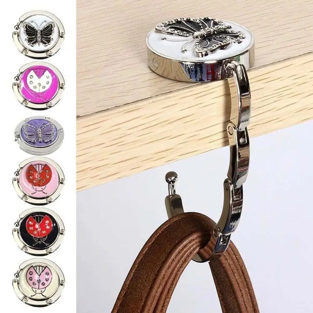 Gancho de soporte para mesa en forma de mariposa plateada, unido a una superficie de madera y correa de cuero.