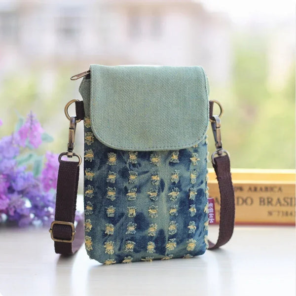 A teal denim mini messenger bag with a flap and strap resting on a white surface.