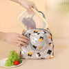 Une main tient un sac à lunch en tissu réutilisable à motif chat et un contenant alimentaire en silicone transparent.