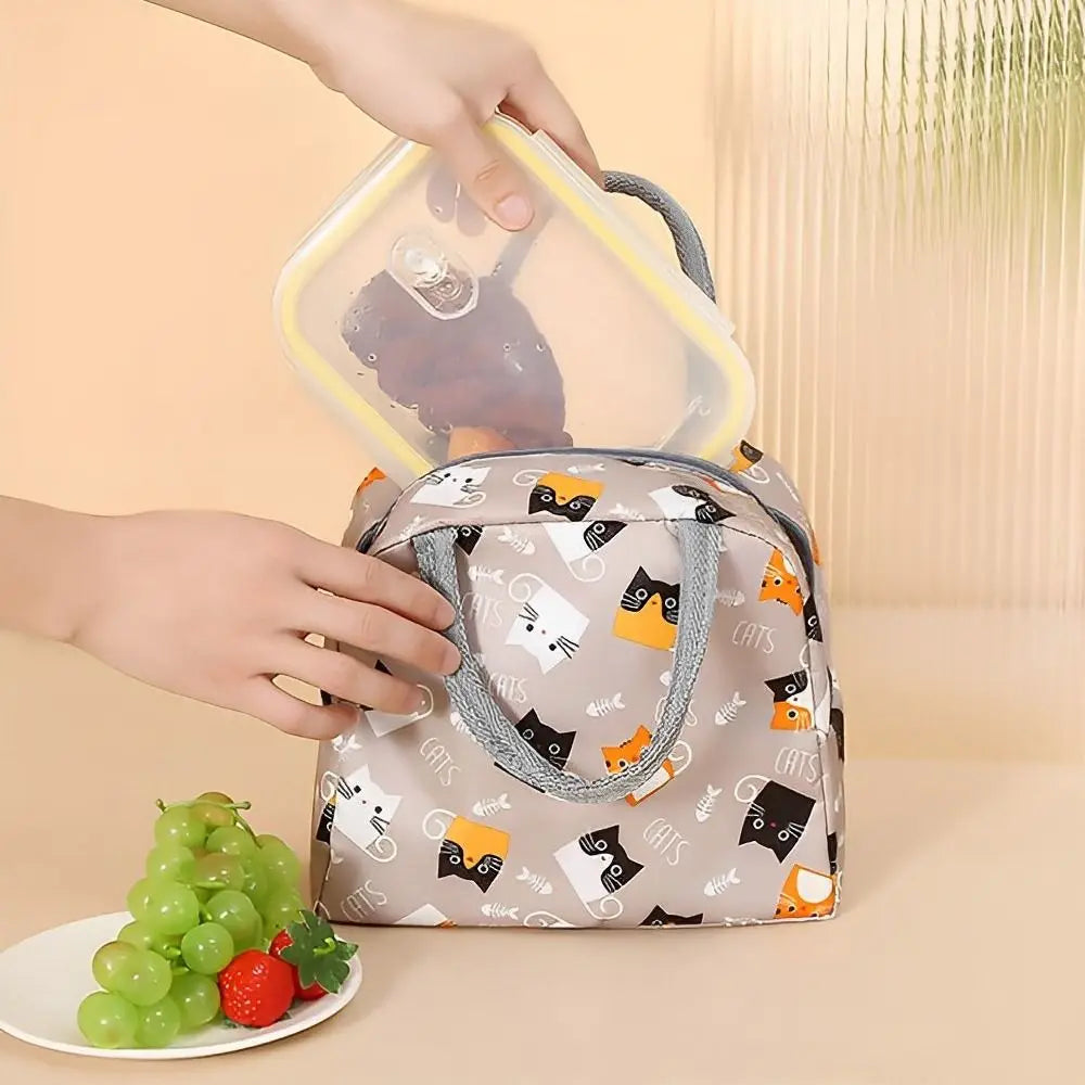 Une main tient un sac à lunch en tissu réutilisable à motif chat et un contenant alimentaire en silicone transparent.