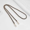 A close-up of a black and gold chain strap with adjustable buckles lying on a white surface.