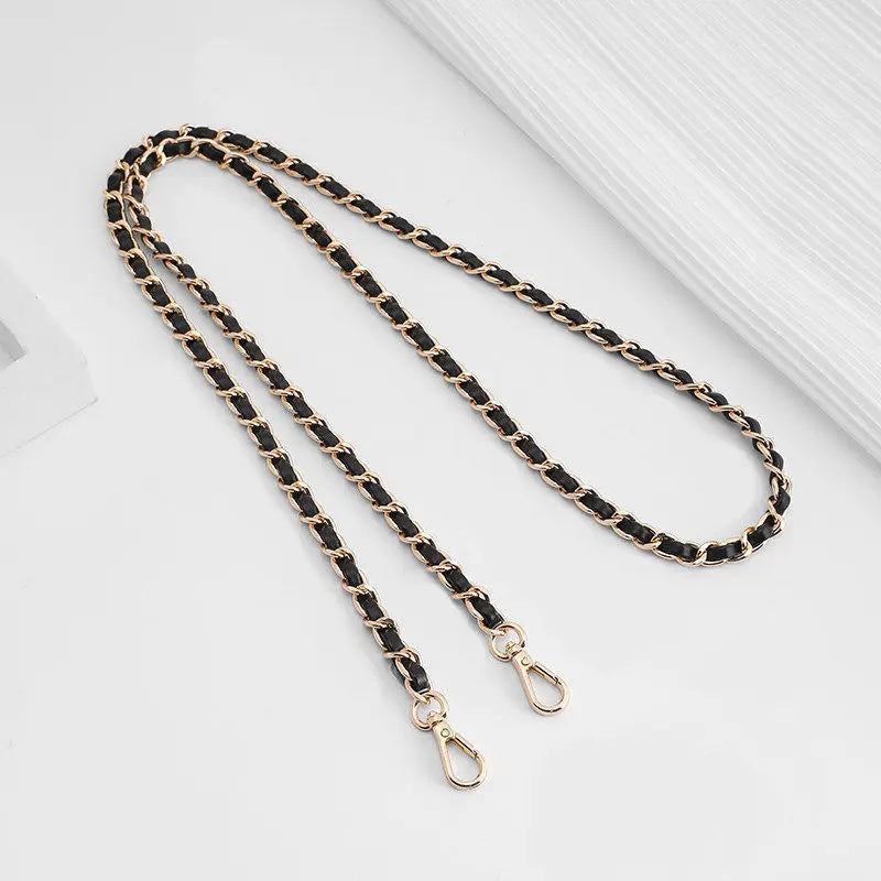 A close-up of a black and gold chain strap with adjustable buckles lying on a white surface.