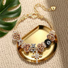 A gold chain bracelet featuring leopard print and black beads with a cross charm displayed on a gold tray.