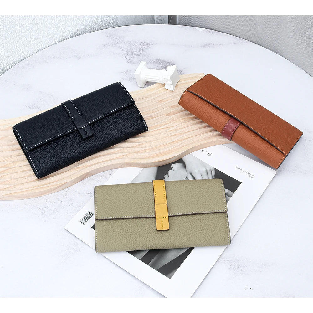 A display of three genuine cow leather bifold wallets in black, brown, and olive green on a light wooden board.