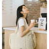 A woman carrying a beige large capacity tote bag and a coffee cup while commuting.