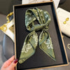 A dark olive green paisley silk hair scarf and headband displayed in a black frame.