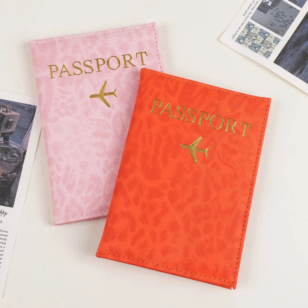 Two pink and orange leopard print PU leather passport holders with gold foil text and airplane emblems.