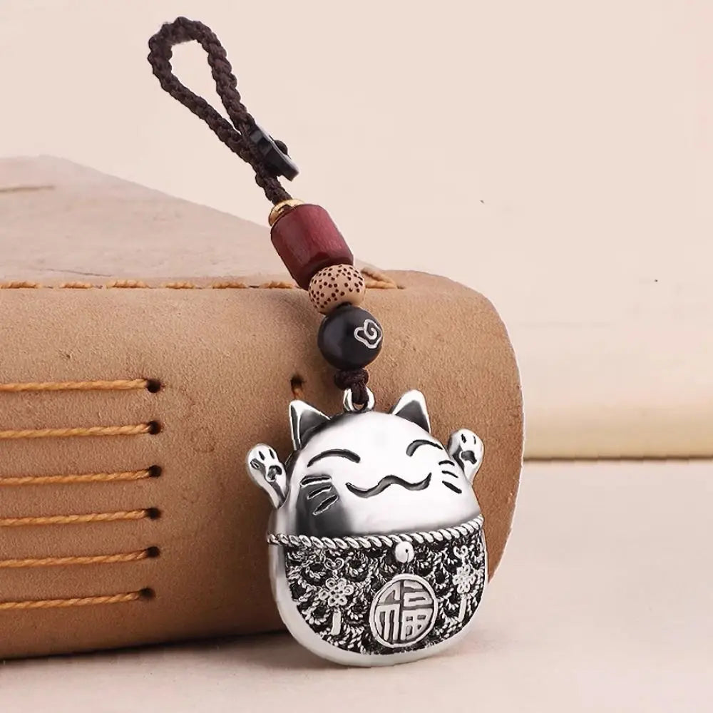Silver lucky cat keychain with a traditional Chinese design charm attached to a dark brown leather pouch.