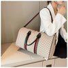 A woman holds a beige plaid travel duffle bag with black and red trim against a light background.