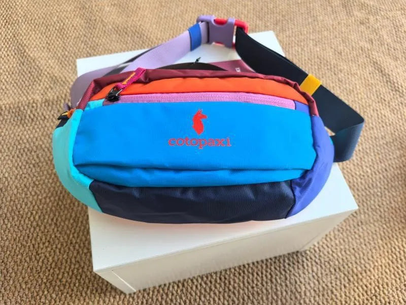 Bunte, strapazierfähige Outdoor-Sport-Crossbodytasche mit mehreren farbigen Fächern auf einer weißen Box.