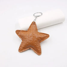 Colgante de llavero con forma de estrella de cuero marrón y anillo plateado, mostrado sobre fondo blanco.