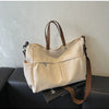 A beige lightweight nylon tote bag with brown leather handles and multiple pockets resting on a black surface.